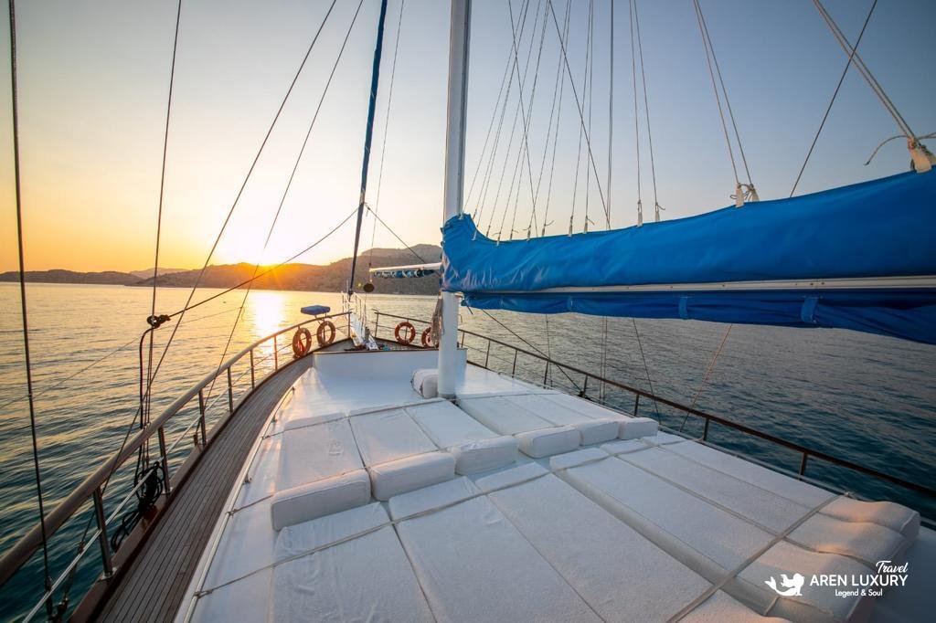 Expansive forward sunbathing deck on Gulet Gokce with plush white sun loungers and blue sail details at sunset.