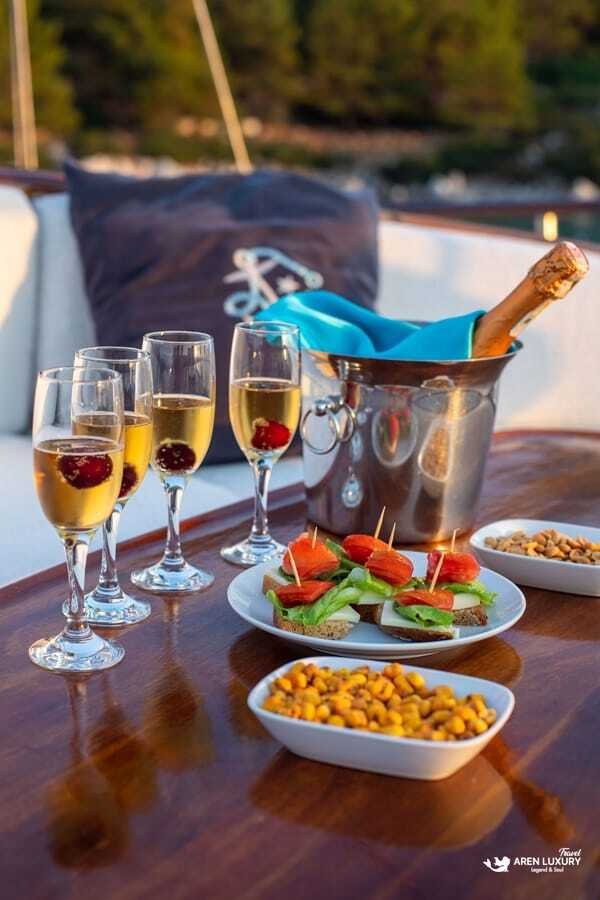 A long mahogany dining table on the aft deck of Gulet Gokce, set with white linens, turquoise runners, and crystal glassware at sunset.