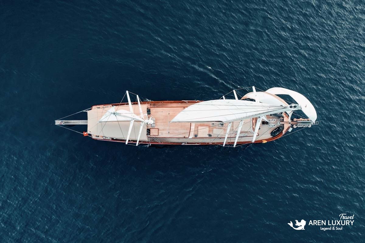 Direct overhead aerial view of La Bella Vita gulet showing the wooden deck layout and white sails against dark blue water.