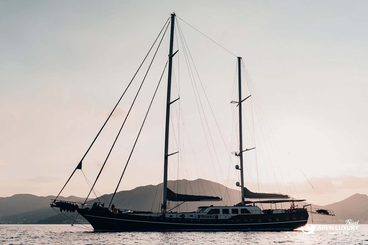 Side profile of luxury gulet La Bella Vita at anchor during sunset with mountains in the background.