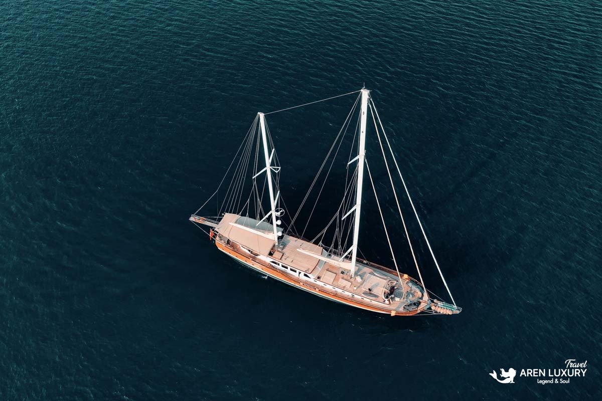 High-angle aerial view of luxury gulet La Bella Vita sailing on dark blue water, showcasing its full deck and white sails.