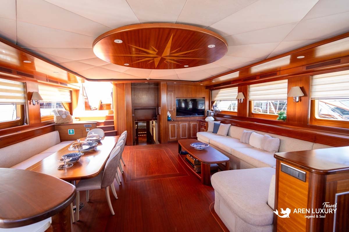 Wide-angle view of the luxury gulet La Bella Vita main salon with wood paneling, cream sofas, and a dining area.