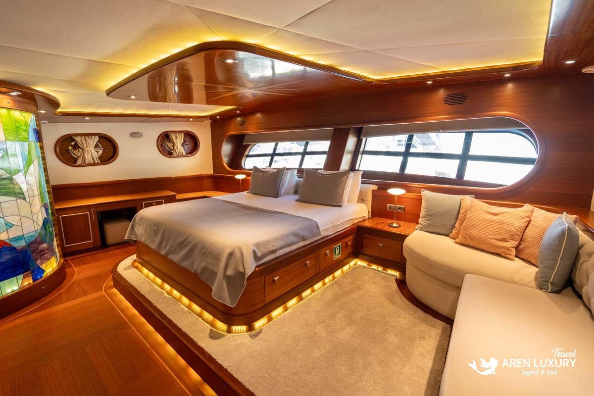 Main salon of Gulet La Bella Vita featuring a white L-shaped sofa, wooden dining table, and the captain's helm station.