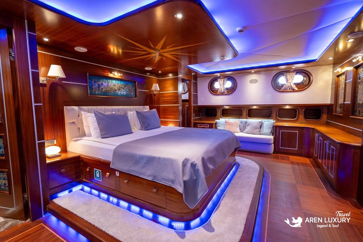 VIP master suite on a luxury gulet featuring a large double bed with blue LED under-lighting, polished wood walls, and a private seating area.