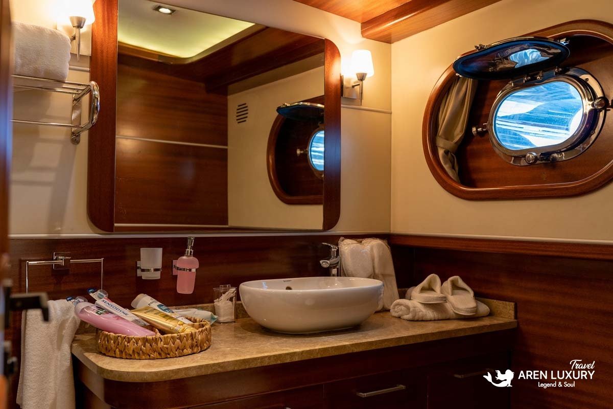 Modern ensuite bathroom on La Bella Vita luxury gulet featuring a white vessel sink, marble countertop, and traditional nautical porthole windows.