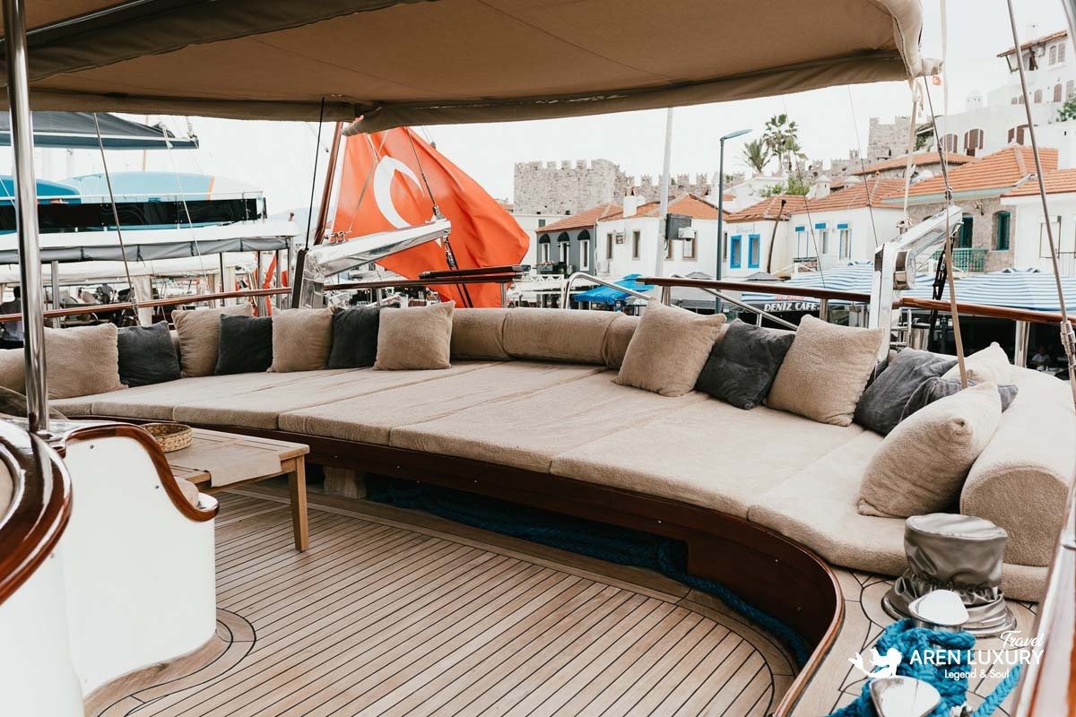 Spacious aft deck lounge of La Bella Vita gulet with comfortable sun cushions, overlooking Bodrum harbor and the historic castle.