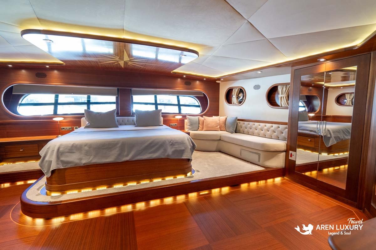 Master suite of La Bella Vita luxury gulet in Bodrum featuring a large double bed with warm LED under-lighting, a plush cream sofa, and mahogany wood interiors.