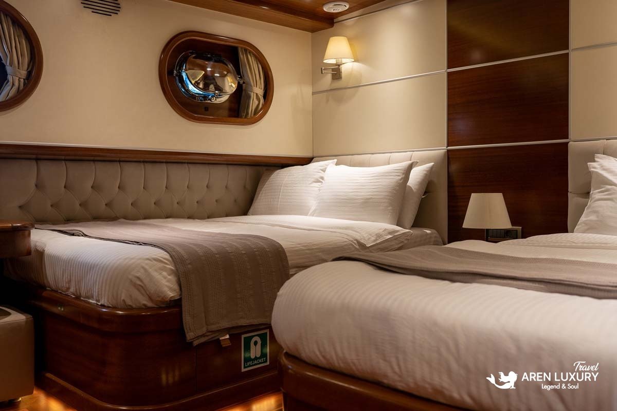Luxury twin guest cabin on La Bella Vita gulet featuring two single beds with premium white linens, mahogany wood paneling, and warm under-bed LED lighting.