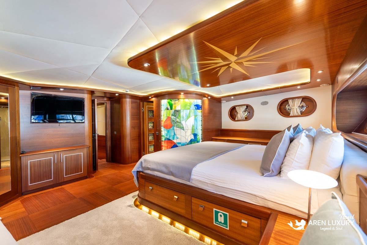 VIP master suite on La Bella Vita luxury gulet featuring a large double bed with gold LED under-lighting, a starburst wood ceiling inlay, and a colorful stained-glass ensuite entrance.