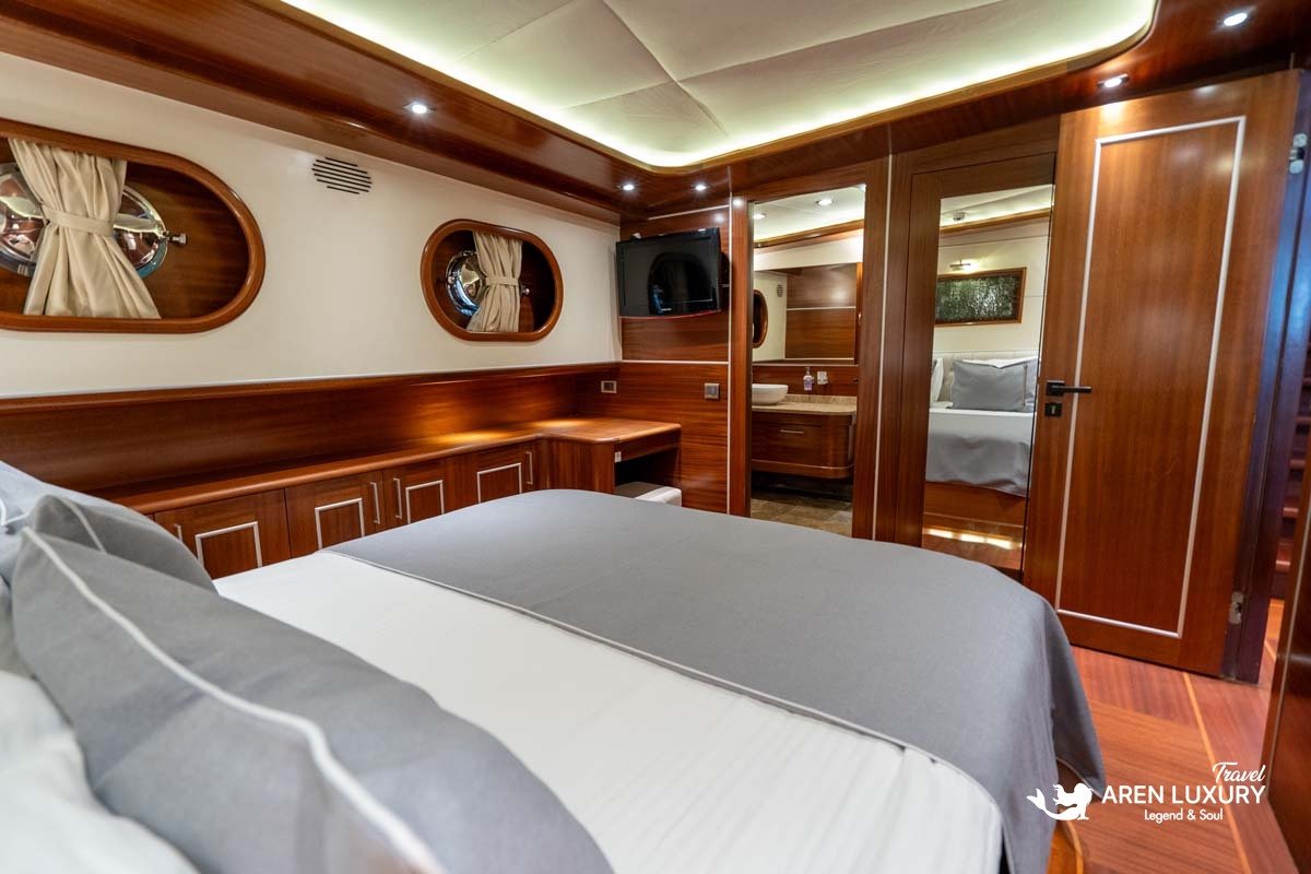 Modern double guest cabin on a luxury gulet with mahogany wood paneling, a wall-mounted TV, and a view into the private ensuite bathroom.
