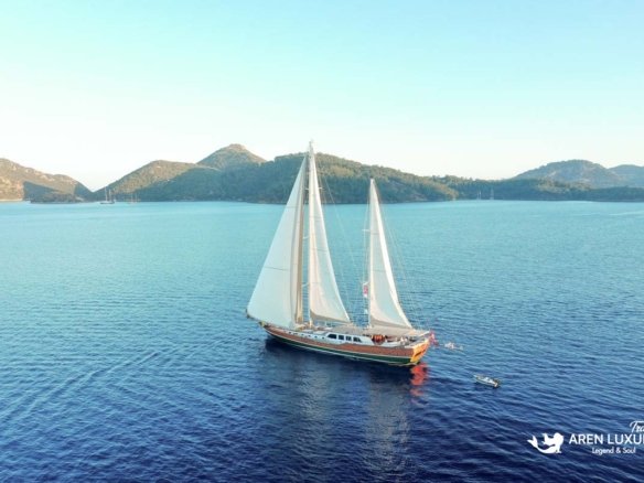 Wide aerial shot of luxury gulet La Bella Vita sailing on calm turquoise waters near a green coastline.