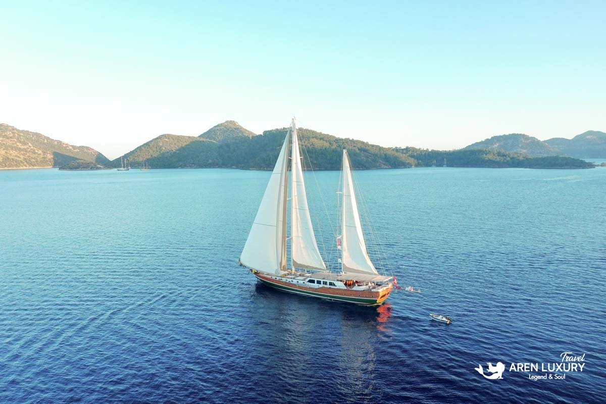 Wide aerial shot of luxury gulet La Bella Vita sailing on calm turquoise waters near a green coastline.